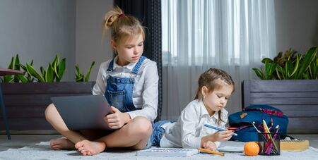 Two sisters lying on the floor at living room using laptop, playing and drawingの写真素材