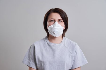 Young woman wearing surgical mask for protection from coronavirus over grey background with copy spaceの写真素材