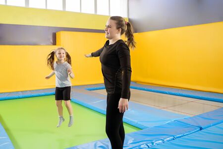 Female trainer helping girl warming up and preparing to workout on trampoline