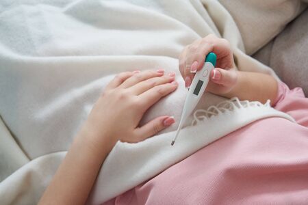 Woman looking at thermometer. Female hands holding a digital thermometer. Concept of fever, flue or...