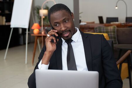 Closeup of angry young african man screaming while talking on smartphone over grey backgroundの写真素材
