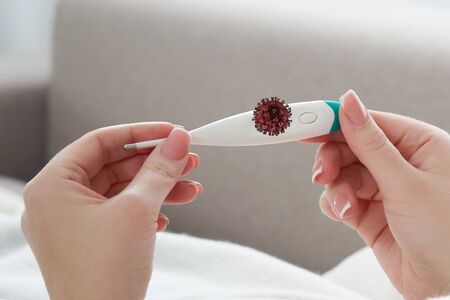 Female hands holding thermometer with coronavirus sign on a screen