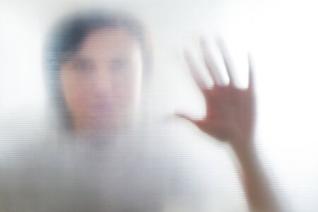 Diffused silhouette of female hands through frosted glass