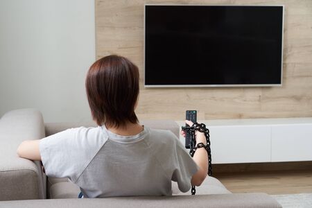 Remote control dependency concept. Female hand tied to the remote with the chainの写真素材