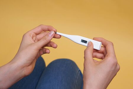 Woman looking at thermometer. Female hands holding a digital thermometer. Concept of fever, flue or...