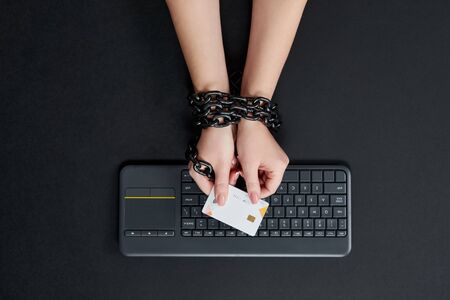 Woman with metal chain holding credit card over keyboard, online shopping addiction conceptの写真素材