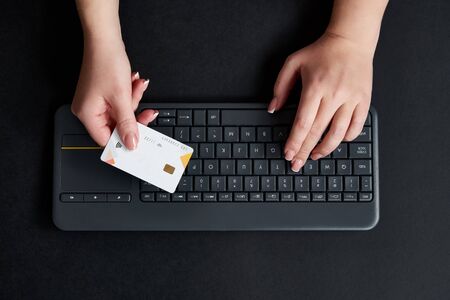 Woman holds credit card and does online payment with computer. Online shopping concept, view from aboveの写真素材