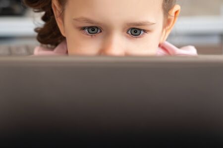 A close up of a little girl looking at a laptop or tablet with copy space