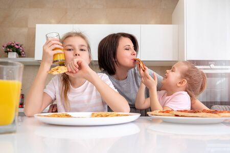 Mother and two daughters eating homemade pizza at a table in kitchen, happy family conceptの写真素材