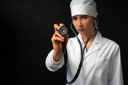 Cropped view of young female doctor holding stethoscope hanging on her neck, studio shot over black...