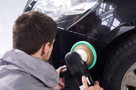 Man using polisher to polish black car body in the workshop