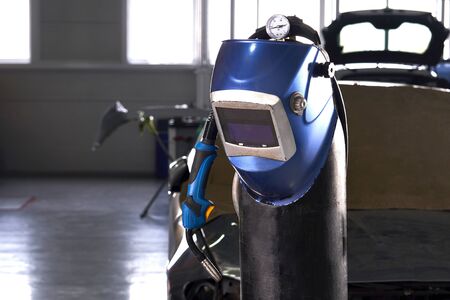 Welding equipment in a car repair station, helmet hanging on a gas tank, no people