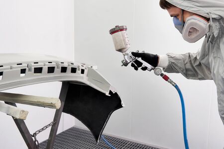 Mechanic painting bumper of a car with sprayer in painting booth in repair auto service