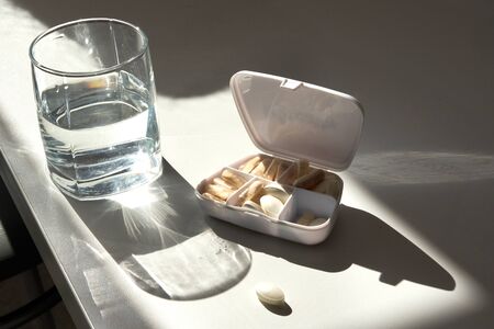 Glass of Water and Pills on white tableの写真素材