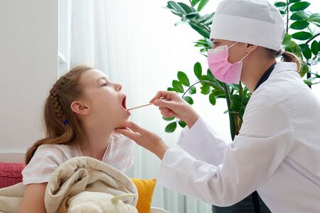 Childrens doctor examining little girls throat at home with a tongue depressorの写真素材