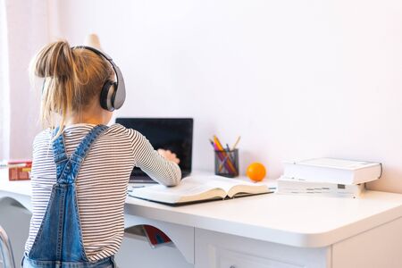 Portrait of teenage girl learning online with headphones and laptop taking notes in a notebook...