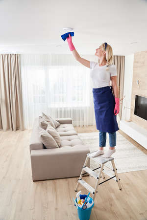 Maid woman holding mop pile, cleaning ceiling in living room. House cleaning service concept.の写真素材
