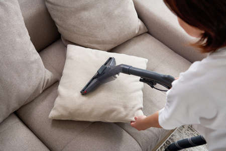 Young housewife Cleaning Sofa with Vacuum Cleaner in living roomの写真素材