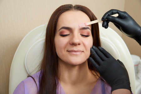 Pretty girl getting brow waxing in beauty salon