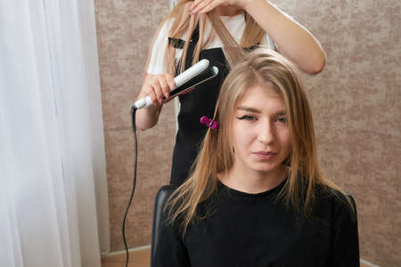 Hairstylist working on woman client with crimperの写真素材
