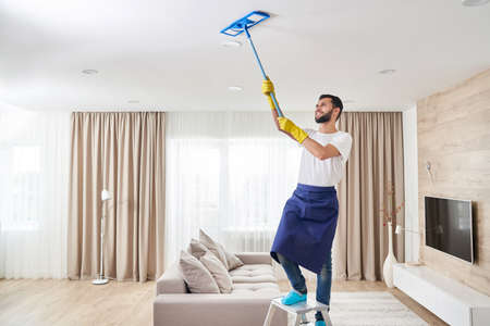 Man cleaning ceiling and lamps in living room. House cleaning service concept.の写真素材