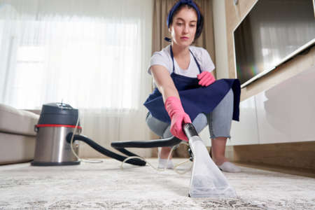 Woman Cleaning Carpet In The Living Room Using Vacuum Cleaner At Home. Cleaning service conceptの写真素材