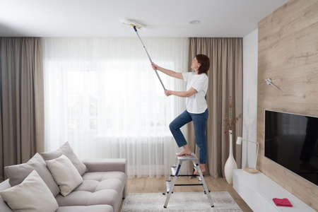 Woman cleaning ceiling with a mop. Housewife cleaning living roomの写真素材