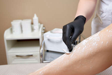 Beautician getting ready to wax female legs in spa center. Preparation for depilation, putting on some white powderの写真素材