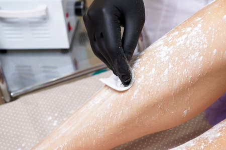 Beautician getting ready to wax female legs in spa center. Preparation for depilation, putting on some white powderの写真素材