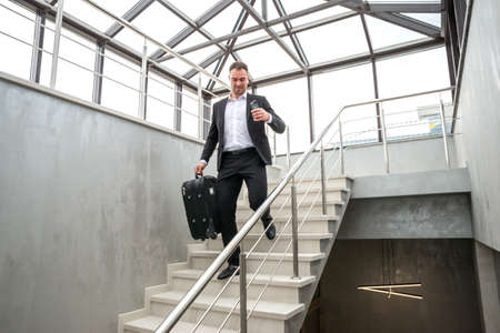 Businessman holding suitcase running on stairs in modern building