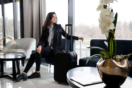 Woman sitting with suitcase in hotel lobby or in an airport loungeの写真素材