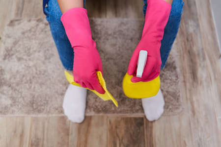 Tired woman in rubber gloves sitting on a toilet and holding cleaning spray. Top viewの写真素材