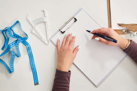 Nutritionist doctor writing diet plan on table with measuring tape, view from aboveの写真素材