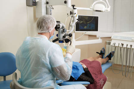 Dentist working with dental microscope and patient at modern dentist clinic