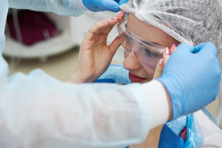 Dentist puts protective glasses on patient woman before teeth cure in dentistry
