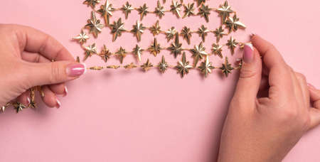 Female hands making design of golden Christmas tree with star on pink background. View from above. Flat layの写真素材