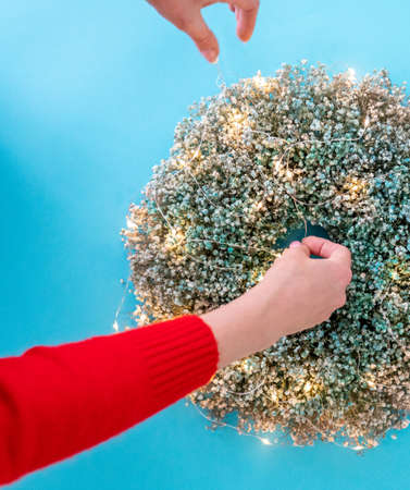 Female hands decorating christmas wreath with garland, top viewの写真素材