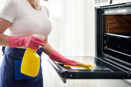 Young woman wearing gloves cleaning oven in the kitchen. Cleaning service conceptの写真素材