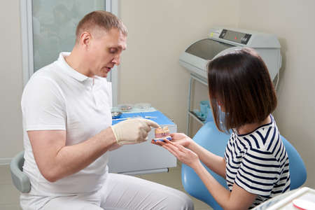 Male dentist showing his female patient a dental implant