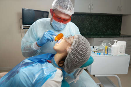 Dentist doing procedure with dental curing UV light in clinic