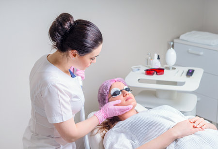 Young woman receiving laser treatment in cosmetology clinic. Eyes covered with protection glassesの写真素材