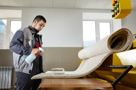 Man wearing uniform Spraying Detergent On blue Carpet To Remove Stain in professional cleaning serviceの写真素材