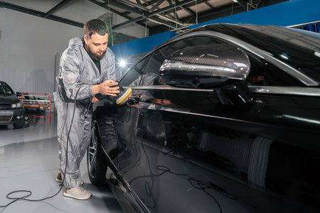 Worker polishing car with special grinder and wax from scratches at the car service station....