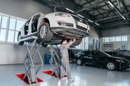 Mechanic repairing Car on lift in mechanic shop or garage, interior of auto repair workshopの写真素材