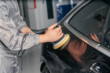 Worker polishing car with special grinder and wax from scratches at the car service station. Professional car detailing and maintenance conceptの写真素材