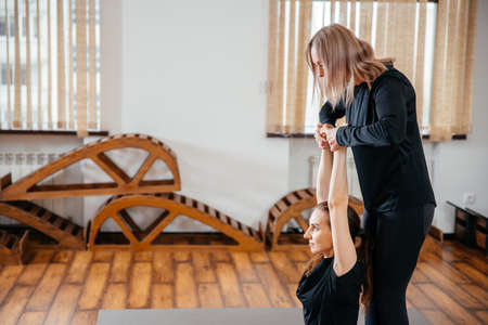 Yoga teacher is helping young woman to make poses at gymの写真素材