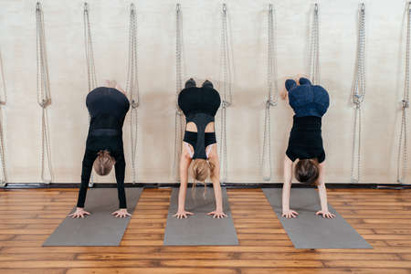 Women learning to stand on hands near wall in studio. Upside down yoga position