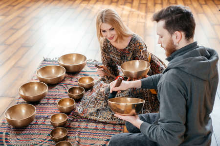 Woman and man playing on a tibetian singing bowl for sound therapy sitting in yoga studioの写真素材