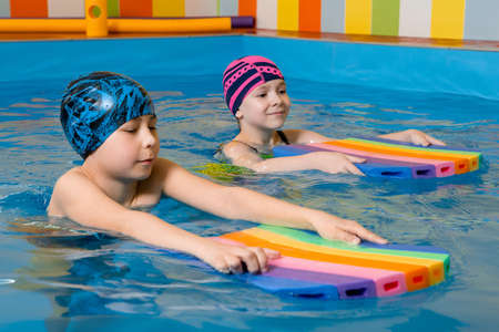 Boy and girl wearing swimsuit uses a foam pad to practice swimming in swimming poolの写真素材