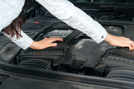 Young woman standing in front of the car with opened hood looking under car hoodの写真素材